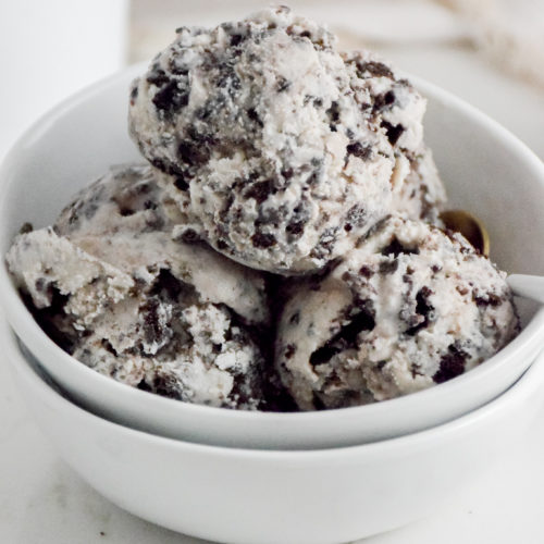 Cookies 'n Cream Ice Cream Scoops in a white bowl on a white background with crumbles cookies on either side