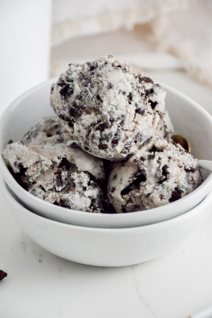 Cookies 'n Cream Ice Cream Scoops in a white bowl on a white background with crumbles cookies on either side