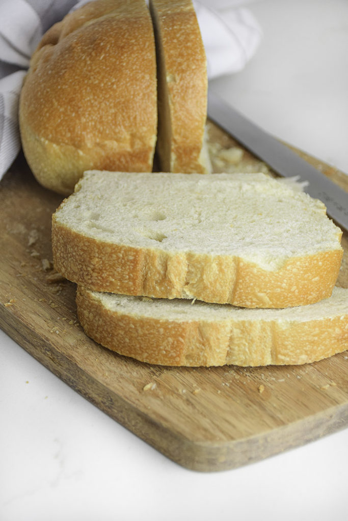 thick slices of white bread on a wooden cutting board loaf of bread and knife in the beackground