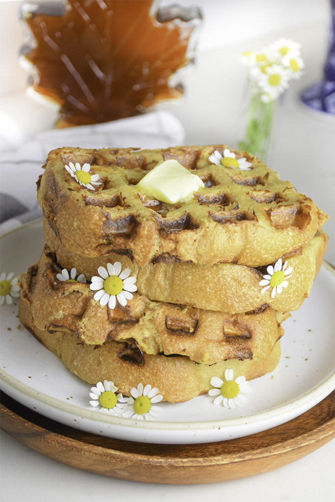 stack of french toast waffles on a white plate with pat of butter on top and chamomile flowers