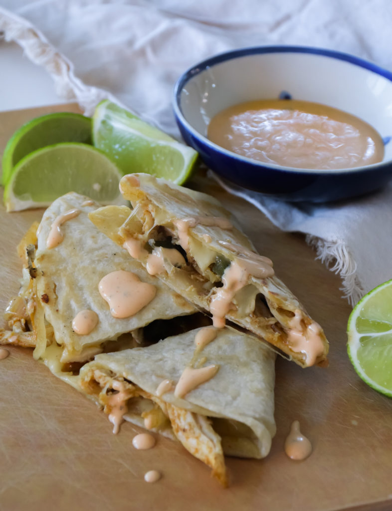 Quesadillas on a light brown surface with Cholula Ranch drizzle and small blue and white bowl