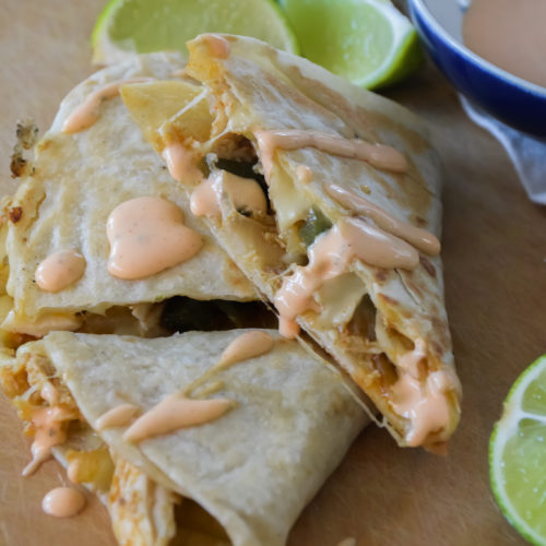 Quesadillas on a light brown surface with Cholula Ranch drizzle and small blue and white bowl