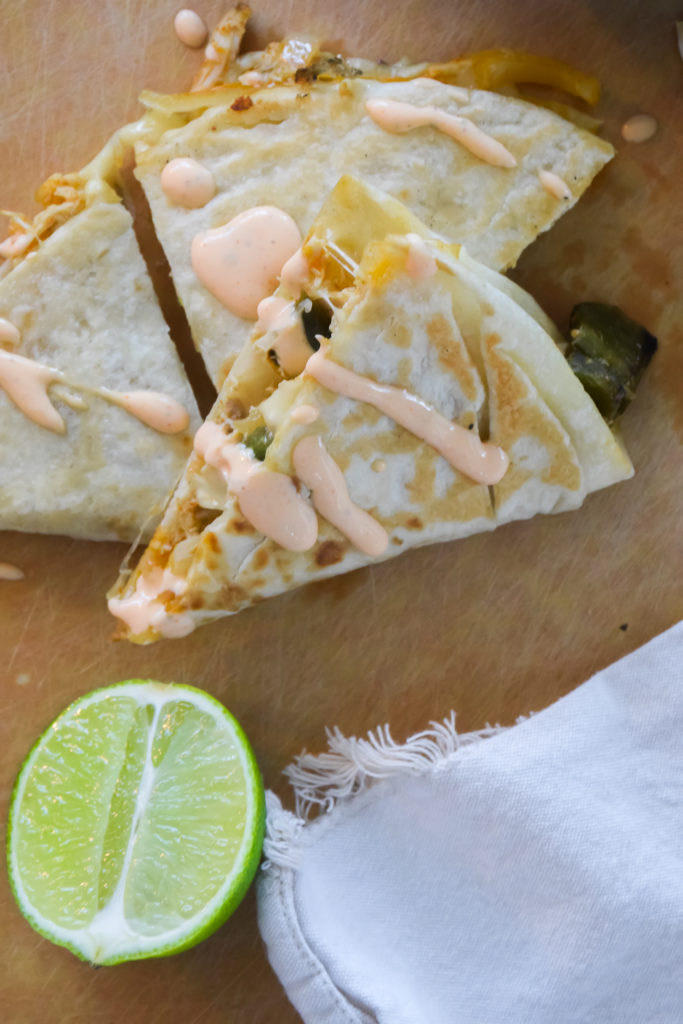 Quesadillas on a light brown surface with Cholula Ranch drizzle and small blue and white bowl