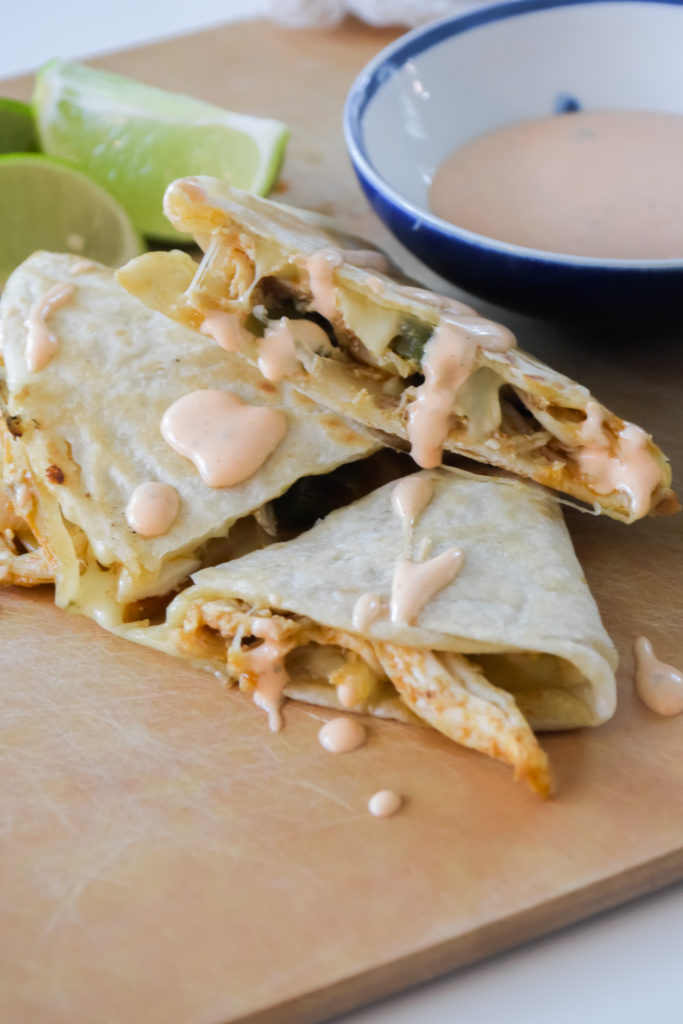 Quesadillas on a light brown surface with Cholula Ranch drizzle and small blue and white bowl