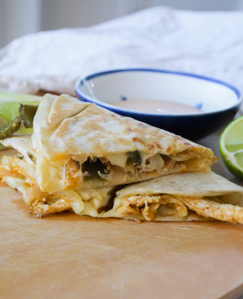 Quesadillas on a light brown surface with Cholula Ranch drizzle and small blue and white bowl