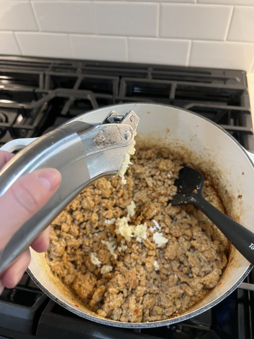 browned meat in white pot on a stove with garlic press