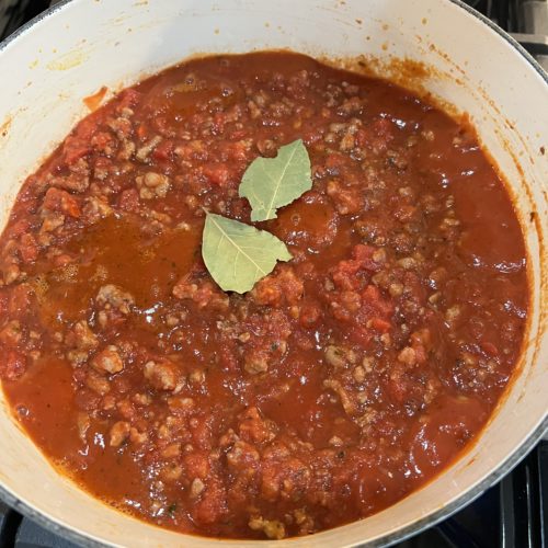 red sauce in a white pot on stove with two bay leaves on top