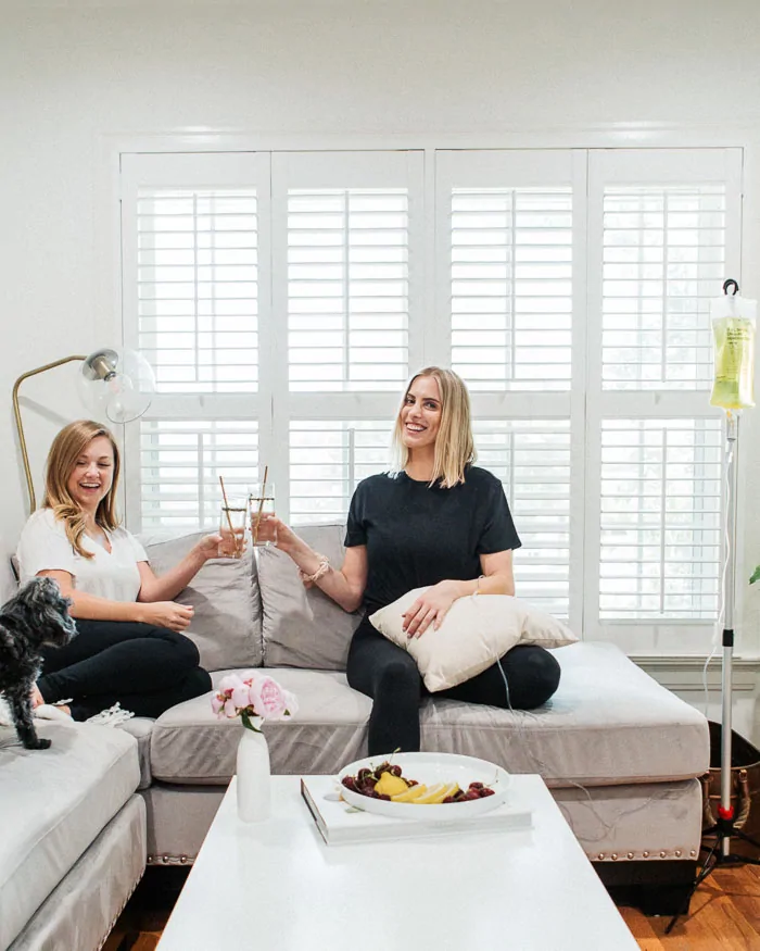 two women sitting on couch cheersing glasses