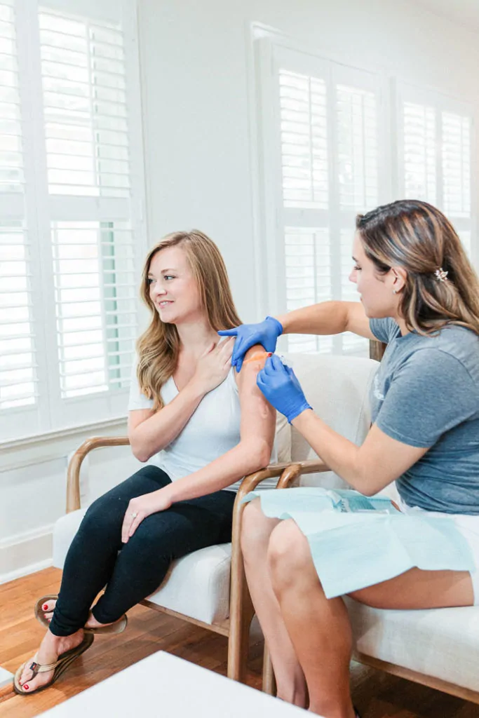 woman sitting in chair getting shot from nurse with blue medical gloves on