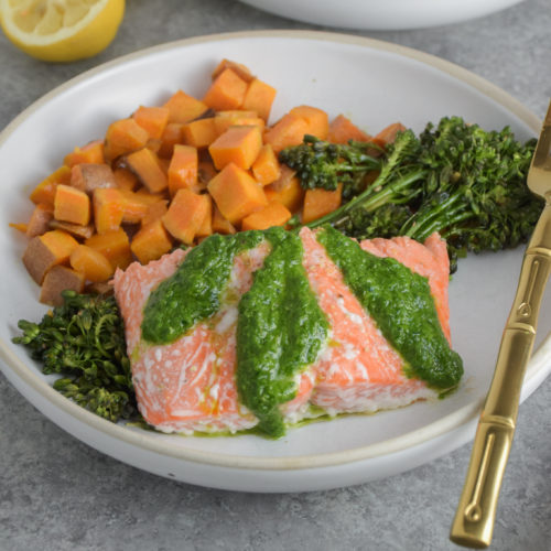 Salmon with green basil pesto on white plate with broccolini and sweet potatoes