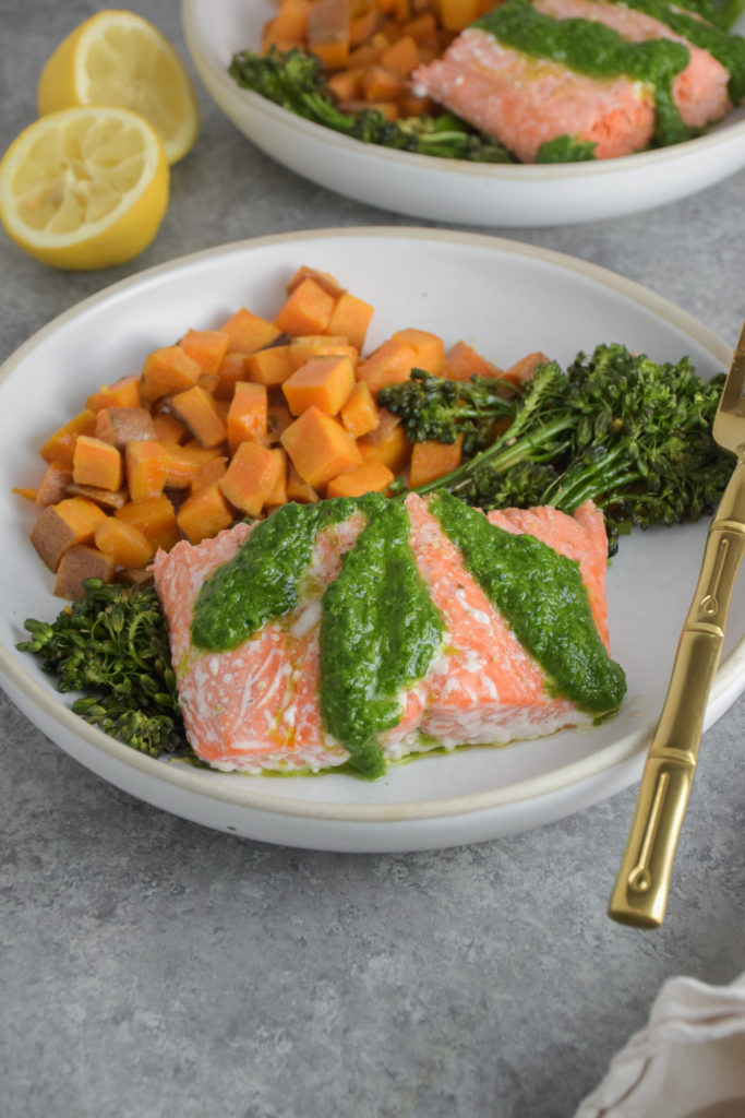 Salmon with green basil pesto on white plate with broccolini and sweet potatoes