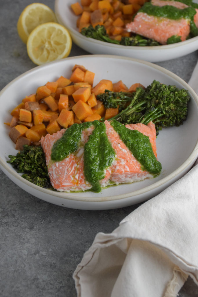 Salmon with green basil pesto on white plate with broccolini and sweet potatoes