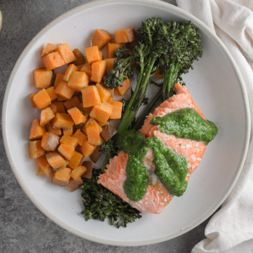 Salmon with green basil pesto on white plate with broccolini and sweet potatoes