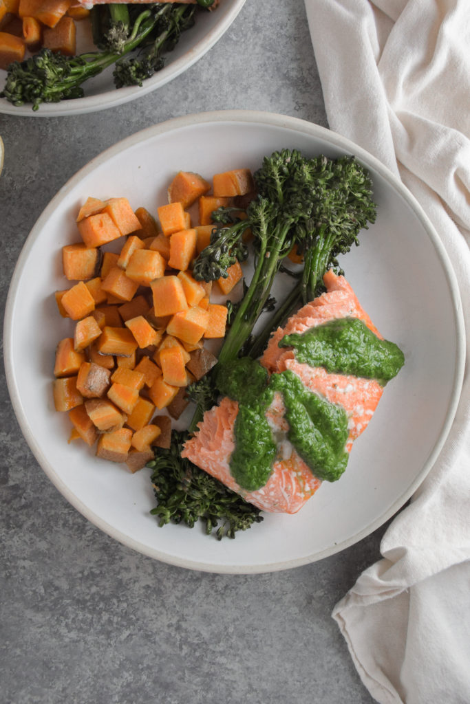 Salmon with green basil pesto on white plate with broccolini and sweet potatoes