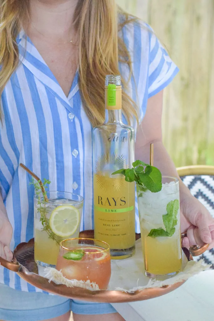 Woman with striped blue and white shirt holding copper tray with three different types of cocktails 