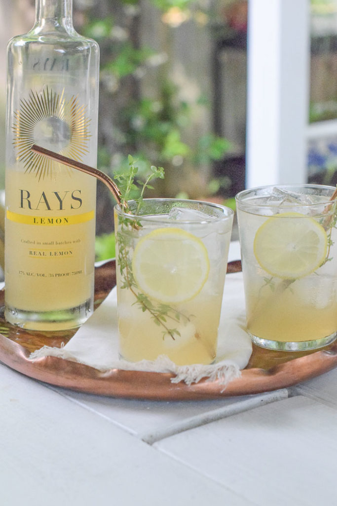 Two glasses of lemonade cocktail with fresh lemon slices and thyme sprigs on a copper tray with Rays lemon bottle 